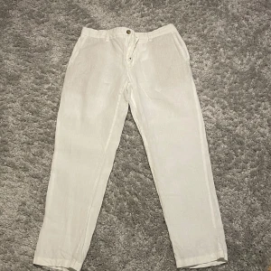 Vita linnebyxor från Dressmann - Snygga vita linnebyxor från Dressmann i ren linne. Byxorna har raka ben, bälteshällor, sidfickor och bakfickor med knapp. Perfekta för en fräsch och stilren look under varmare dagar.