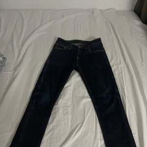 Mörkblå jeans från Nudie Jeans Co - Snygga mörkblå jeans från Nudie Jeans Co i klassisk femficksmodell. Jeansen har raka ben, kontrastsömmar och är tillverkade i slitstarkt denim. Perfekta för dig som gillar en tidlös och clean look.