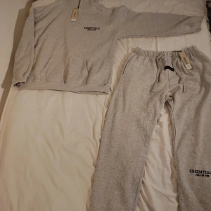 Grå mjukisbyxor Essentials Fear of God - Grå mjukisbyxor från Essentials Fear of God med elastisk midja och snörning. Byxorna har en relaxed passform, muddar vid bensluten och logga tryckt på benet. Perfekta för en chill och avslappnad stil. Materialet är mjuk bomullsmix.