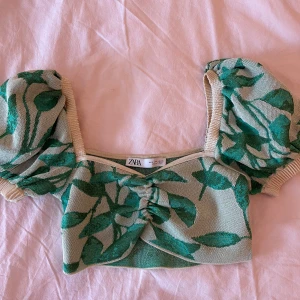Grön blommig croppad topp från Zara - Superfin croppad topp från Zara med grönt blommigt mönster på beige botten. Toppen har puffiga korta ärmar med ribbade muddar och snygg rynkdetalj framtill. Storlek S men passar mig som bär XS. I fint skick.
