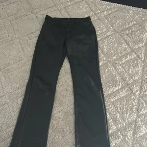 Svarta skinnbyxor från BikBok - Snygga svarta byxor i skinnimitation från BikBok, raka ben och klassisk femficksmodell. Byxorna har bälteshällor och knappstängning framtill. Perfekta för dig som vill ha en edgy look med stilren vibe.