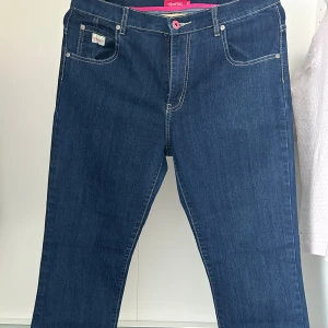 Blå 90-tals jeans från Memories by Olé - Snygga blå jeans från Memories by Olé med klassisk femficksdesign och kontrastsömmar. Jeansen har raka ben, normal passform och cool detalj med rosa knapp och rosa insida i midjan. Bakfickorna har broderad dekor. 