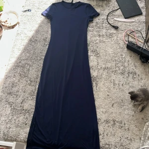 Mörkblå långklänning i stretch - Enkel och stilren mörkblå långklänning från H&M i stretchigt material. Klänningen har rund halsringning, korta ärmar och en figurnära passform som ger en clean look. Perfekt för dig som gillar minimalistisk stil och vill ha något bekvämt men snyggt.