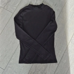 Svart ribbad polotröja från Monki - Svart polotröja från Monki i storlek XS. Tröjan är ribbad med lång ärm och har en enkel, clean design med hög hals. Materialet är mjukt och stretchigt för skön passform.