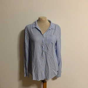 Blårandig skjorta från H&M L.O.G.G. - Klassisk skjorta med blå och vita ränder från H&M L.O.G.G. Skjortan har lång ärm, bröstficka och knappar framtill. 