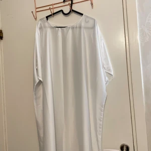 Vit långklänning i satin med pärldetaljer - Elegant vit långklänning i glansigt satinliknande material med vida ärmar. Klänningen har rund halsringning och är dekorerad med pärl- och paljettkant längst ner på ärmarna för en extra touch.  Maxi klänning så om du är 165+ är den perfekt