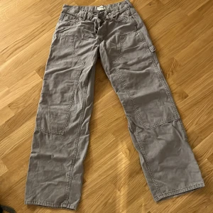 Grå cargopants med raka ben - Säljer ett par grå cargopants med raka ben och flera stora fickor på sidorna. Byxorna har en avslappnad passform och är tillverkade i bomull, vilket gör dem både bekväma och slitstarka. Perfekta för en chill och streetig stil.