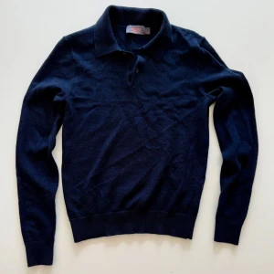 Mörkblå kashmir pikétröja - Snygg mörkblå pikétröja från Morris i mjuk kashmir. Tröjan har klassisk krage, knäppning vid halsen och långa ärmar. Perfekt för dig som gillar stilrena och bekväma plagg med exklusiv känsla.