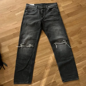 Svarta slitna jeans med raka ben - Svarta jeans med coolt slitna knän och raka ben. Jeansen har klassisk femficksdesign och en tvättad, något blekt look. Perfekta för dig som gillar en avslappnad och edgy stil.