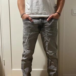 Grå jeans med straight fit - Säljer ett par grå jeans med rak passform och klassisk femficksdesign. Jeansen har en snygg tvättad look och är tillverkade i bomull. Perfekta för dig som gillar en enkel och stilren stil.