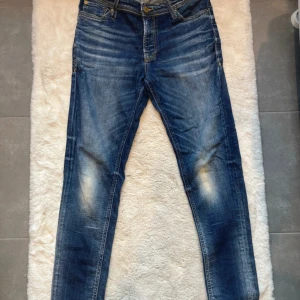 Blå jeans från Jack & Jones - Säljer ett par blå jeans från Jack & Jones med snygga slitningar och kontrastsömmar. Klassisk femficksmodell med normal passform och raka ben. Jeansen har en cool tvättad look och är tillverkade i bomullsmaterial.
