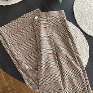 Rutiga kostymbyxor från Zara - Snygga kostymbyxor från Zara i klassiskt rutig mönster med beige, bruna och svarta toner samt tunna röda linjer. Byxorna har medelhög midja, raka ben och hällor för bälte. Oanvända samt långa (jag är 177cm lång)