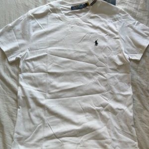 Vit t-shirt från Polo Ralph Lauren - Klassisk vit t-shirt från Polo Ralph Lauren med broderad logga på bröstet. T-shirten har rund hals, korta ärmar och är gjord i mjuk bomull. Perfekt basic-plagg med snygg passform och stilren look.