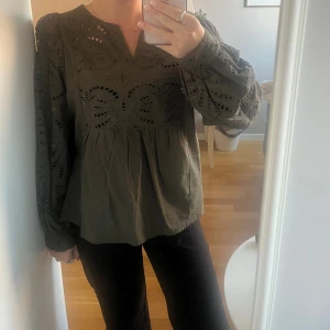 Olivgrön blus med broderade detaljer - Olivgrön blus med v-ringning och långa puffärmar. Blusen har broderade hålmönster över bröstet och ärmarna, samt en lös passform passform. Perfekt för alla olika tillfällen! Använd en gång, fint skick! Från märket cream. Storleken är som en xs/s 