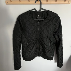 Svart quiltad bomberjacka Magiano - Quiltad svart jacka från Magiano med dragkedja framtill och två fickor med dragkedja. Jackan har en klassisk bombermodell med ribbade muddar och ett stilrent rutmönster. Perfekt som höstjacka. Storlek 40 men passar även 36/38 om man vill inte vill ha den så tajt.