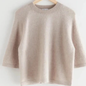 Beige stickad tröja med trekvartsärm - Mysig beige stickad tröja från & other stories med rund halsringning och trekvartsärmar. Tröjan har en enkel och stilren design, perfekt för lager-på-lager och passar till många olika outfits.