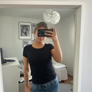 Svart basic t-shirt från Hm - Enkel svart t-shirt med rund hals och korta ärmar från Hm. Den har ett hål i ena ärmen. 