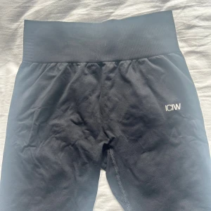 Svarta leggings från ICANIWILL - Svarta leggings från ICANIWILL med hög midja och diskret logga på höften. Stretchigt material som sitter tight och formar sig efter kroppen. Perfekta för träning eller chill, med ribbad midja och mesh-detaljer längs benen för extra stil.