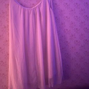 Vit somrig klänning med tunna axelband - Luftig och flowy vit klänning med tunna axelband och vidd i kjolen. Enkel och stilren design med mjukt fallande tyg, perfekt för varma dagar. Klänningen har en rak passform och är ärmlös, vilket ger en avslappnad och fräsch look.