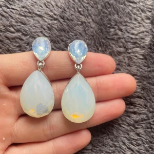 Droppformade örhängen i opalglas🤍 - Stilrena örhängen med stora droppformade stenar i skimrande opalglas. Fästet är också dekorerat med en mindre, facetterad sten i ljusblått. Silverfärgad infattning ger en elegant touch. Perfekta för dig som gillar statement-smycken med glittrig känsla. Som ni ser på vänstra örhänget, så är det lite sönder. Men det är inte något man tänker på, skriv för fler bilder🫶🏻