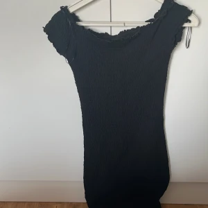 Svart smockad kortklänning Amisu - Säljer en svart smockad klänning från Amisu med kort ärm och offshoulder-design. Änvänd 3gånger