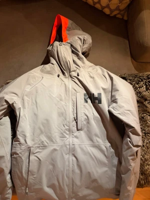 Ljusgrå Helly Hansen powderface - ljusgrå skidjacka från Helly Hansen med svart logga på bröstet. Jackan säljs ej längre. 