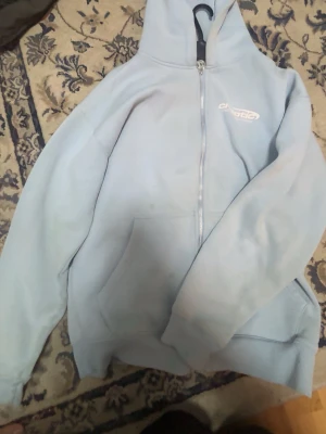 Ljusblå zip hoodie från Chaotic - Snygg ljusblå hoodie med dragkedja från Chaotic. Tryck med texten 'chaotic aesthetic awareness' på bröstet. Klassisk huva och känguruficka framtill. Perfekt för en chill och avslappnad stil. Mjuk bomullsblandning för extra komfort.