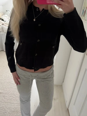 Svart  kofta med knappar - Snygg svart  kofta med rund hals och knäppning framtill. Koftan har långa ärmar och sitter tajt över kroppen. Perfekt att styla med höga jeans eller kjol. Materialet ser ut att vara mjukt och stretchigt.