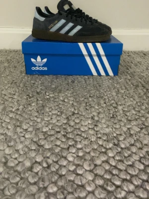 Adidas Spezial sneakers mörkblå mocka - Säljer ett par Adidas Spezial sneakers i mörkblå mocka med ljusblå detaljer och klassiska vita ränder på sidan. Skorna har brun platt sula och snörning framtill. Perfekta för dig som gillar retrostil och streetwear. Skorna är i skick 7av 10 de ändå som behövs är en liten tvät på skorna då de är lite smutsiga. Tveka inte på att höra av dig. Priset går att diskutera😄🙌 obs de till kommer box men är inte orginal boxen