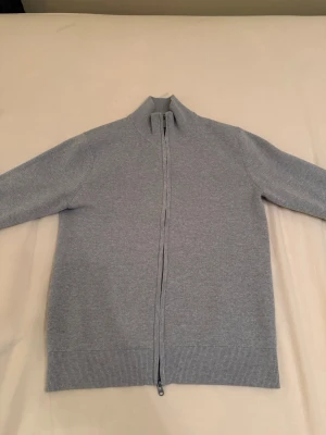 Bläck Zip Tröja - Snygg ljusgrå ziptröja med hög krage och hel dragkedja framtill. Tröjan har långa ärmar och ribbade muddar vid ärmslut och nederkant. Perfekt för lager på lager och enkel att matcha med olika outfits.