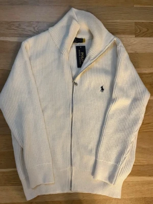 Vit ziptröja från Polo Ralph Lauren - En superunik tröja! Aldrig använd, i nyskick. Tröjan är tjock, varm och perfekt för vintern och höst/vår, både för en fin och bekväm look. Tröjan är för män. Säljer den pägrund av storleken. Den är i storlek M. Modellen på bild 2 är 178cm/72kg. Hör gärna av dig om du har några frågor eller funderingar!