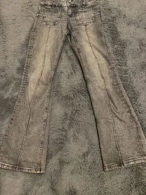 Grå bootcut jeans med framfickor - Snygga grå jeans med bootcut-modell och markerade sömmar längs benen. Jeansen har två stora framfickor och en cool, tvättad look. Perfekta för dig som gillar en retrostil med lite edge.