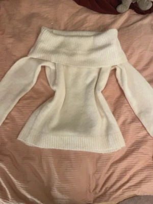 Vit off shoulder stickad tröja - Säljer en vit stickad tröja med bred off shoulder-krage och långa ärmar. Tröjan har ribbstickade detaljer vid krage, ärmslut och nederkant. Perfekt för dig som vill ha en trendig och mysig look.