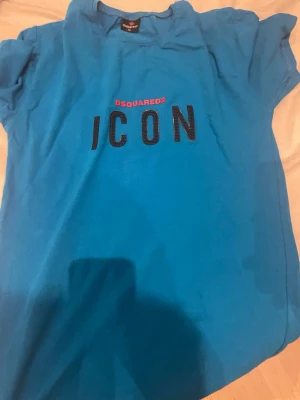 Blå  t-shirt f - Snygg blå t-shirt från Dsquared2 med trycket 'ICON' i svart och rött på bröstet. Klassisk passform med korta ärmar och rund hals. Perfekt för dig som vill sticka ut med ett trendigt statement-plagg.