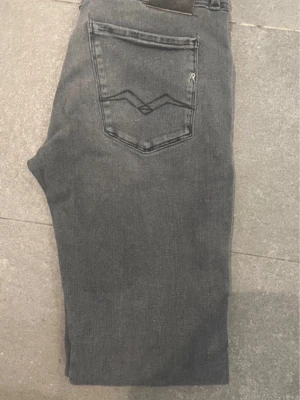 Grå Replay jeans - Säljer ett par grå jeansbyxor från Replay med klassisk bakficka och diskret broderad logga. Jeansen har en rak passform och är tillverkade i mjukt denimtyg som ger en avslappnad look. W30 L34