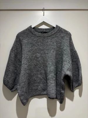 Grå stickad kortärmad tröja  - Mysig grå stickad tröja med rund halsringning och trekvartsärmar. Tröjan har en loose passform och ribbade kanter vid hals, ärmslut och nederkant. 