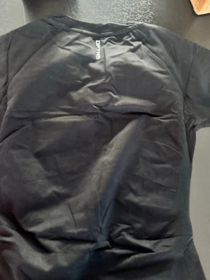 Svart tränings-tshirt från DFYNE - Snygg svart tränings-tshirt från DFYNE med rund hals och korta ärmar. Tillverkad i ett lätt och ventilerande funktionsmaterial som passar perfekt till gymmet eller löprundan. Diskret logga på bröstet och ryggen för en sportig look.