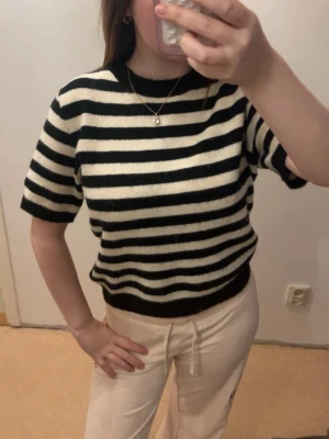 Svartvit randig stickad topp - Superfin stickad topp med svarta och vita ränder. Modellen är kortärmad med rund halsringning och en lite loose passform. Perfekt att styla med både jeans och kjol för en trendig look.