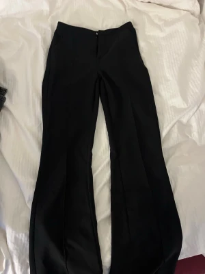 Svarta kostymbyxor med bootcut - Snygga svarta kostymbyxor med bootcut-snitt och mid rise. Byxorna har en stilren look med diskret dragkedja framtill och är perfekta för en clean och trendig outfit. Materialet känns mjukt och följsamt. Sydda till mid rise