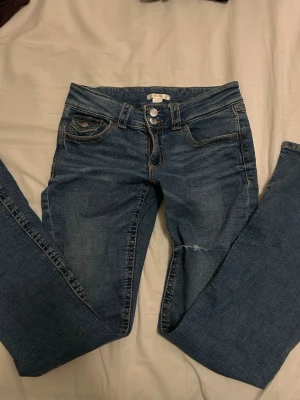 Blå bootcut jeans från Gina Tricot - Snygga blå bootcut jeans från Gina Tricot med klassisk femficksdesign och dubbla silverknappar i midjan. Jeansen har en smal passform och är tillverkade i mjuk bomullsdenim med lite stretch för extra komfort.