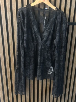 Svart spetsblus med v-ringning - Säljer en svart blus i genombruten spets med v-ringning och långa ärmar. Blusen har ett blommigt mönster i spetsen och är perfekt för dig som gillar en elegant och trendig look. Passar till både jeans och kjol för en snygg outfit.