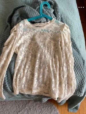 Vit spetsblus med puffärm - Säljer en vit spetsblus med lång ärm och puffdetaljer vid axlarna. Blusen har ett blommigt spetsmönster och rund halsringning. Perfekt för dig som gillar romantisk och feminin stil. Materialet är genombruten spets i polyester.