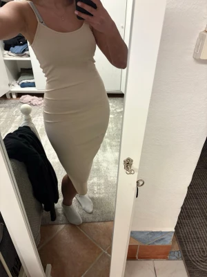 Beige ribbad långklänning - Säljer en beige ribbad långklänning med smala axelband och figurnära passform. Klänningen är ärmlös och har en enkel, stilren design som passar perfekt till sommaren. Materialet känns mjukt och stretchigt för en bekväm känsla.