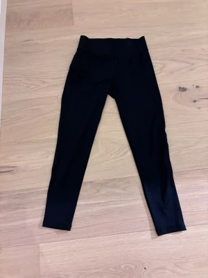Svarta leggings från Newbody - Snygga svarta leggings från Newbody med hög midja och stretchigt material. Perfekta för träning eller chill. De har en enkel, clean look utan mönster och sitter tight mot kroppen. Materialet är en blandning av polyester och elastan för maximal komfort.