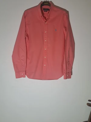 Rosa skjorta Polo Ralph Lauren Slim Fit M - Säljer en rosa långärmad skjorta från Polo Ralph Lauren i slim fit. Skjortan har klassisk krage, knappar framtill och den ikoniska blå broderade loggan på bröstet. Tillverkad i mjuk bomull och passar perfekt för en clean och stilren look.
