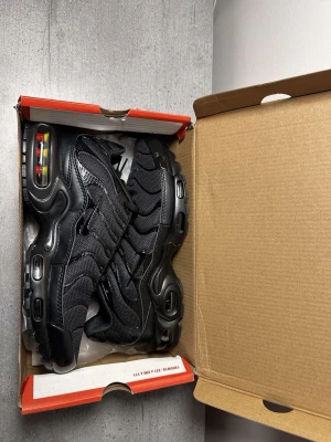 Nike Air Max Plus svarta sneakers - Säljer ett par nya helsvarta Nike Air Max Plus sneakers med mesh- och syntetöverdel, ikoniska vågiga detaljer och synliga Air-enheter i sulan. Skorna har snörning och en chunky, sportig look som passar perfekt till streetwear. Kan tänka mig att gå ner i pris vid snabb affär.