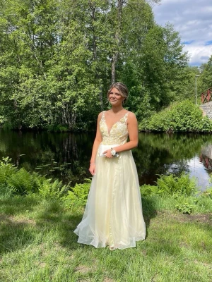 Ljusgul långklänning med spetsdetaljer - Säljer nu min fina balklänning. Den är ljusgul nyans med blommor upp till. Den är insydd vid axelbanden med går att sprätta upp om man vill.🥰