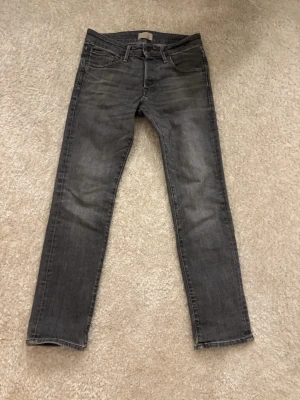 Grå slim jeans i klassisk modell - Snygga grå jeans med smal passform och klassisk femficksdesign. Jeansen har en något tvättad look och raka ben. Perfekta för dig som gillar en stilren och enkel vibe. Slim Glenn storlek 28/30