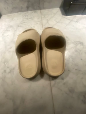 Beige Adidas tofflor i syntet - Säljer ett par beigea yezzy slide tofflor