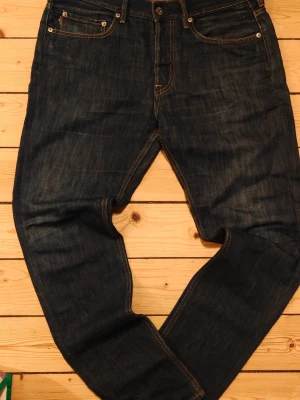 Mörkblå jeans från Stone Island - Snygga mörkblå jeans från Stone Island med klassisk femficksdesign och gul logopatch bak. Jeansen har raka ben och kontrastsömmar som ger en clean look. Perfekta till en avslappnad stil och funkar året runt